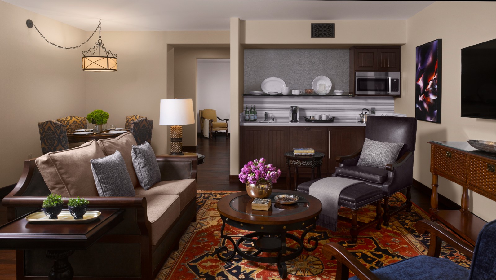 A wide view of a hotel room's living area with sofa, armchair, coffee table, and kitchenette.