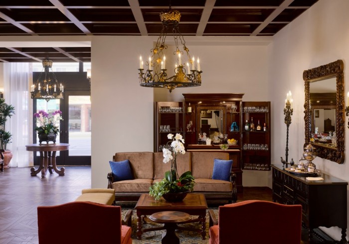 A hotel lobby with a chandelier, sofa, coffee table, armchairs, and bar.